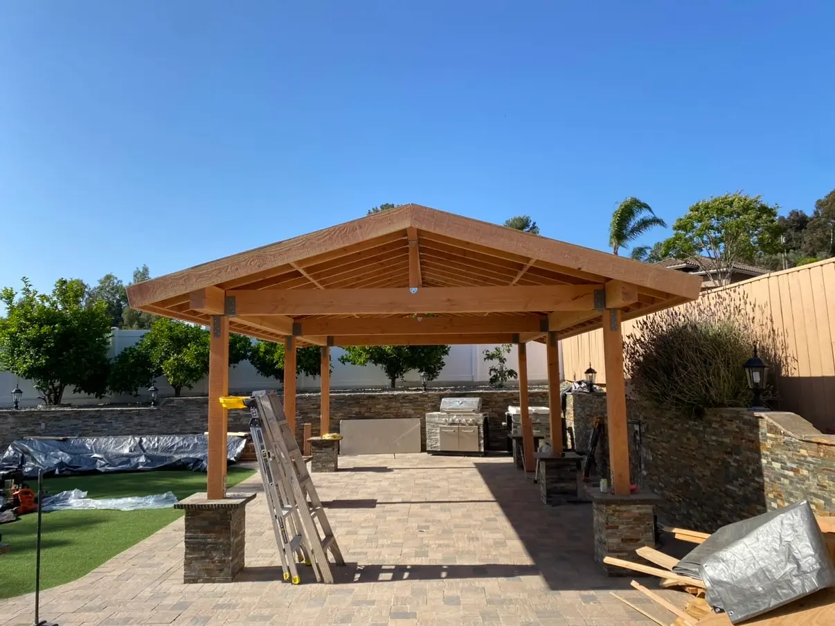 Finished cedar pavilion with a tile roof and stone-clad columns over a paver patio in Rancho San Diego